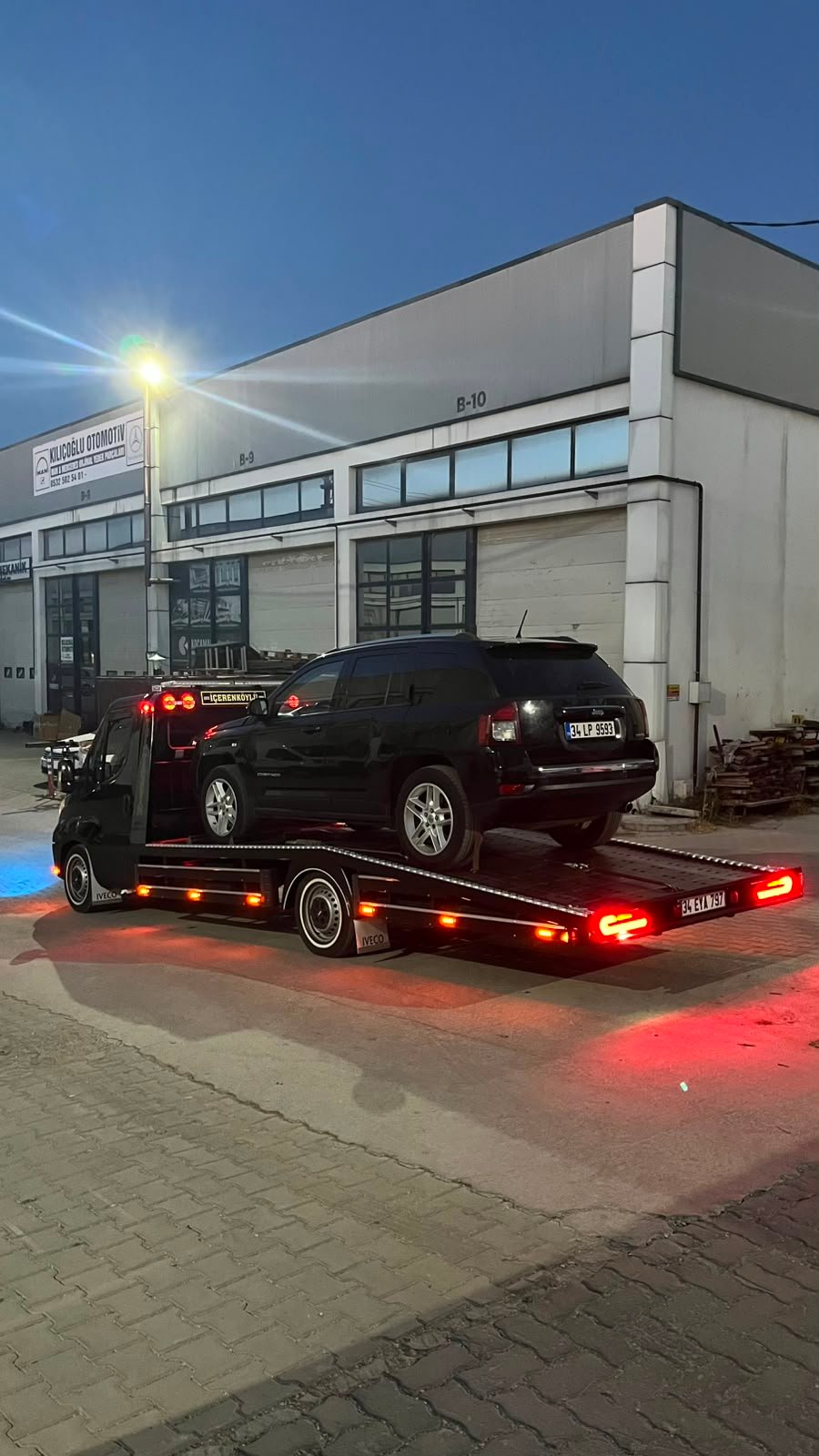 Sanayi alanında platform çekici üzerinde taşınan siyah SUV